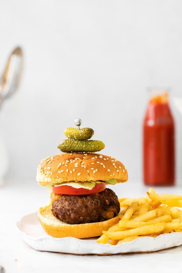 air fryer Juicy Lucy burger sitting on a plate with 2 pickles stuck to the top of the bun. 