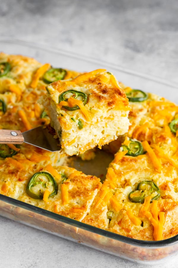 A piece of jalapeño cheddar cornbread being taken out of a 9x13 baking dish.