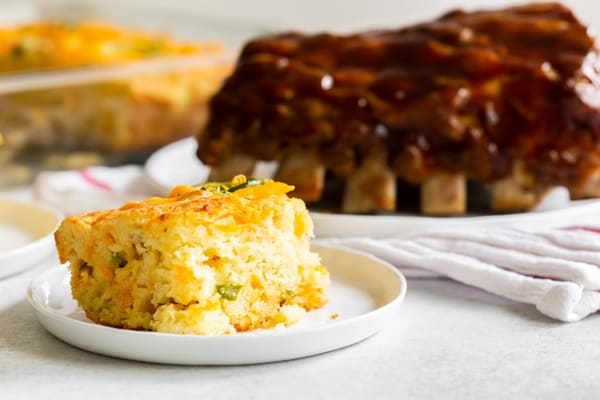 Jalapeño cheddar cornbread on a plate with a rack of ribs in the background. 