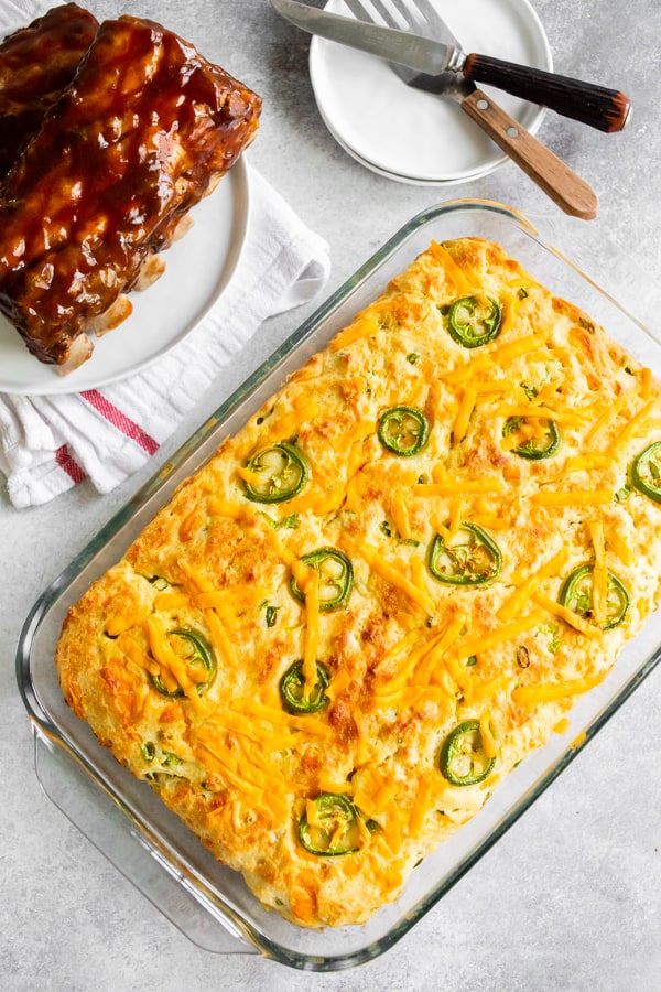 A 9x13 pan of jalapeño cheddar cornbread with a plate of ribs on the side.