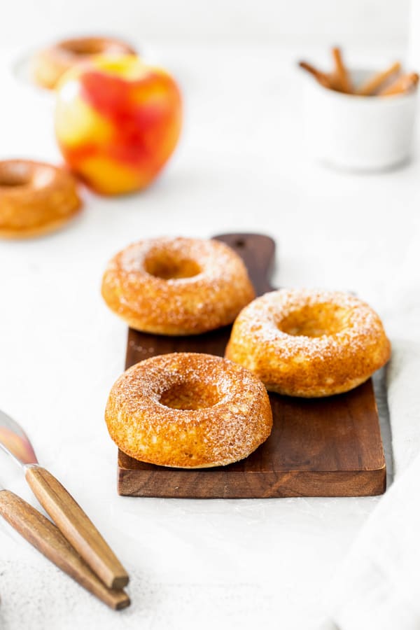Baked apple cider donuts sitting on a cutting board and topped with cinnamon sugar. 