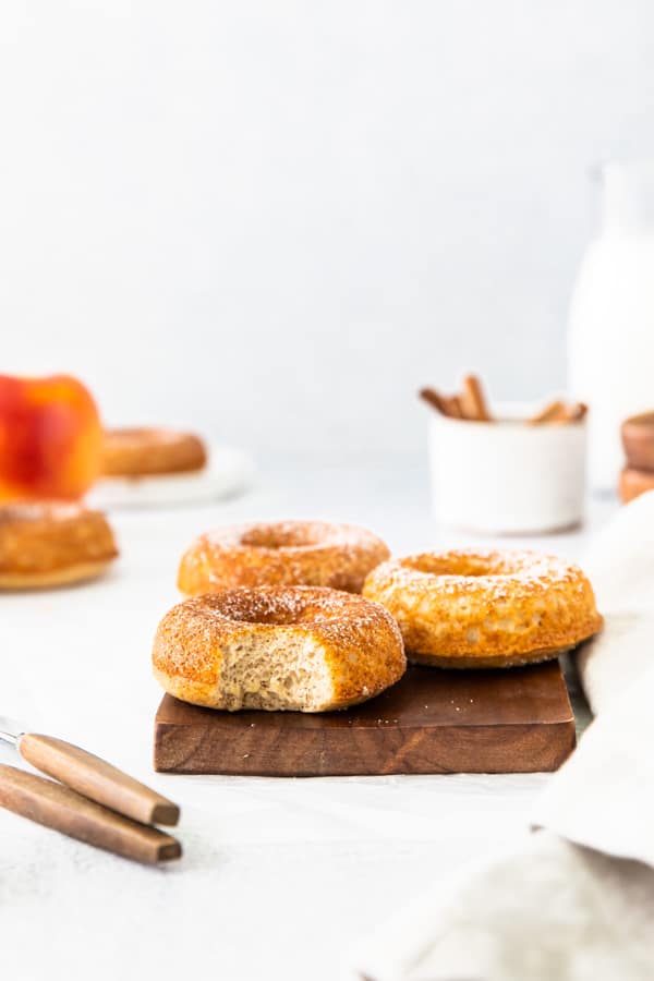 A Baked apple cider donut sitting on a serving board with a bite take out of the donut. 