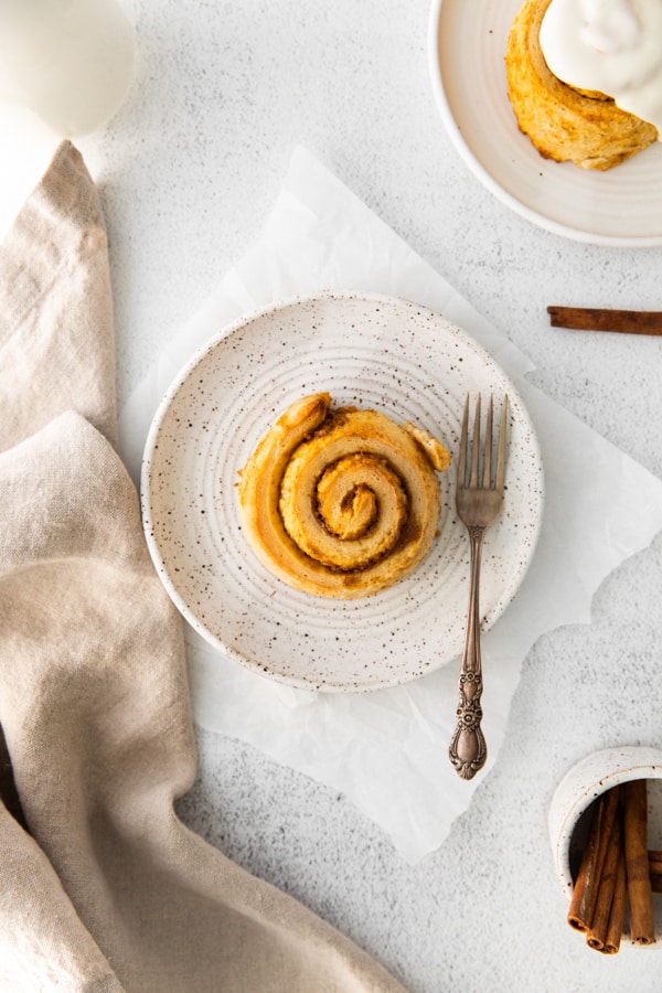 An unfrosted Pumpkin Cinnamon Roll sitting on a plate with a fork.
