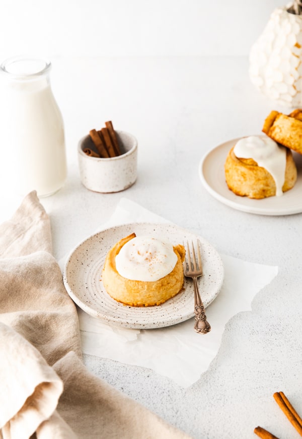 Pumpkin Cinnamon Roll with frosting sitting on a plate.