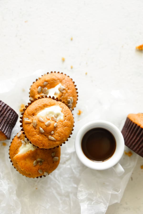 Pumpkin Cream Cheese Muffins sitting on parchment paper with a cup of coffee.