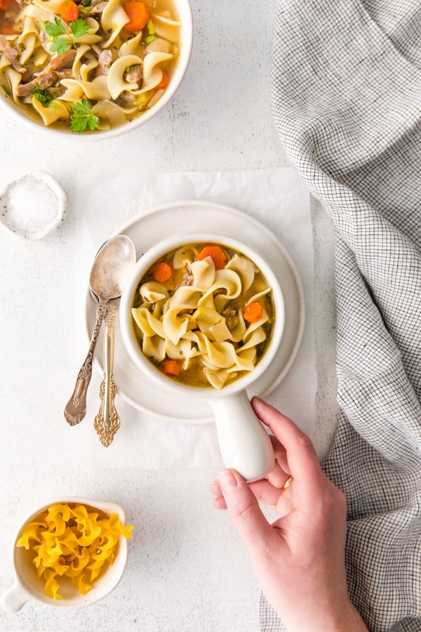 A hand holding a bowl of Instant Pot Turkey Noodle Soup.