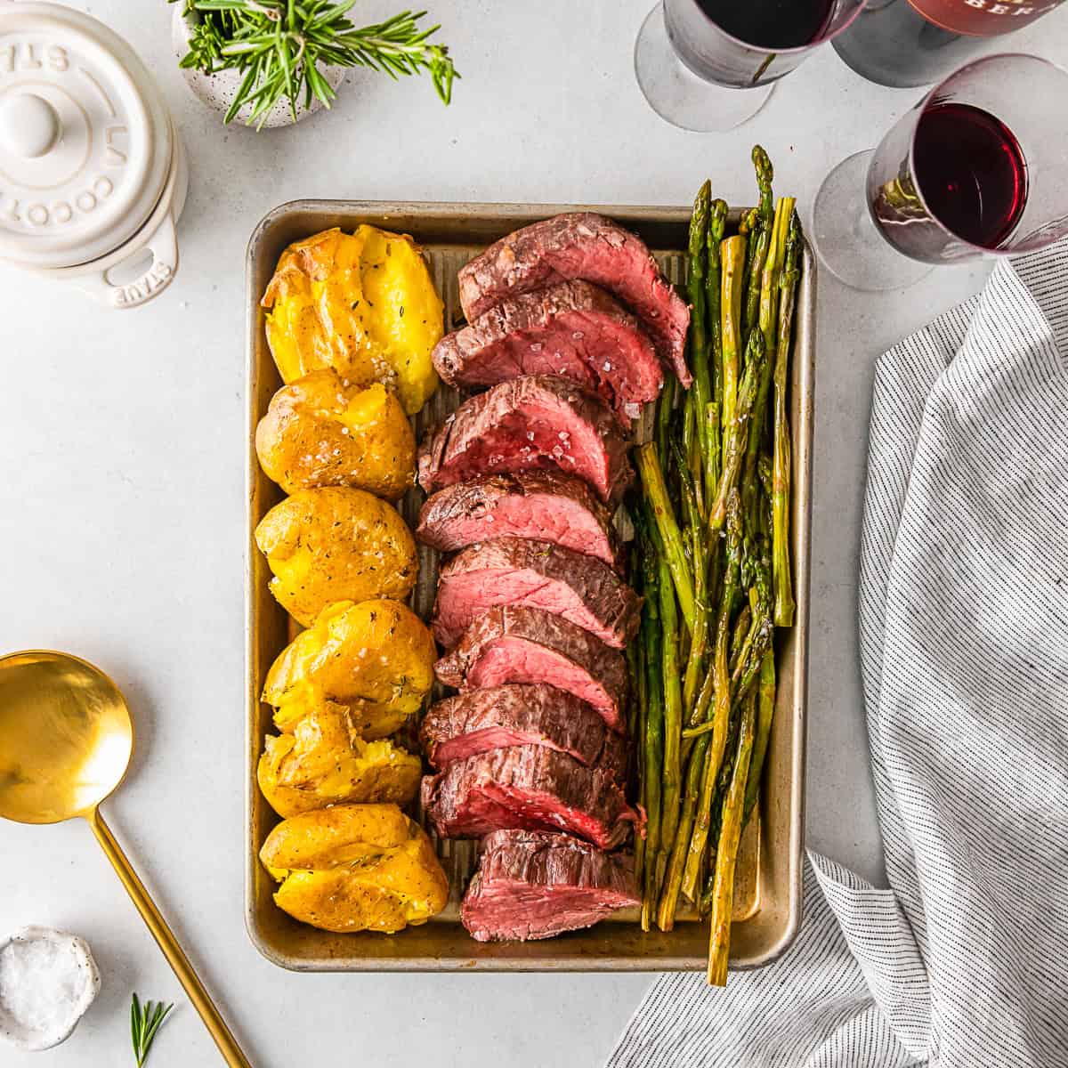Sliced beef tenderloin, potatoes, and asparagus on a sheet pan. 