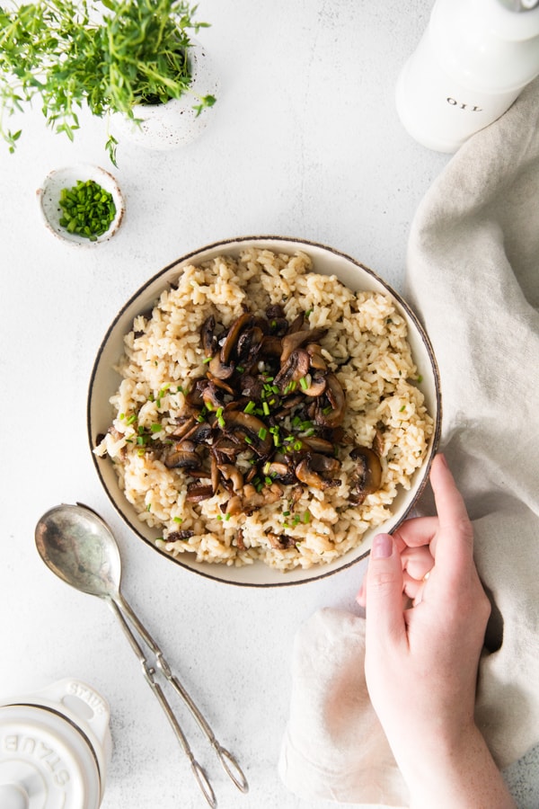 Wild Mushroom Risotto in a bowl with a hand going in to grab the bowl.