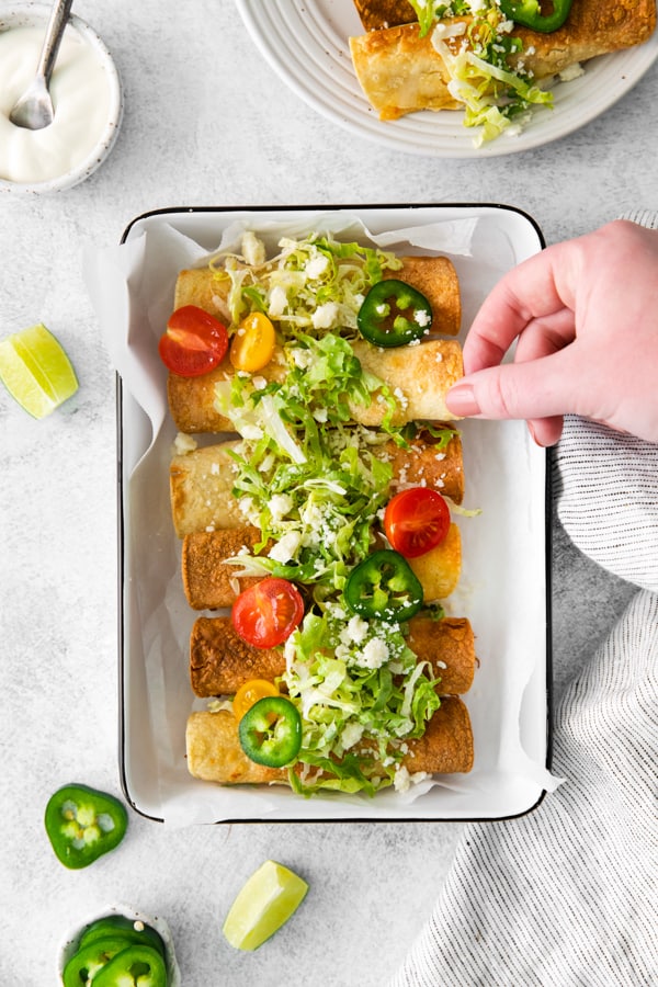 A hand taking an air fryer chicken taquitos.