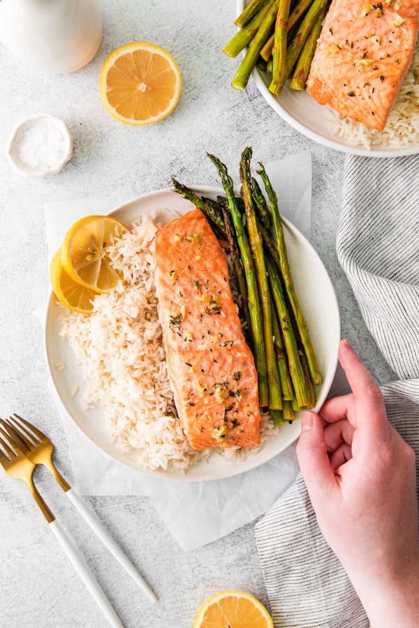 A hand holding a served plate of Sheet Pan Lemon Salmon. 