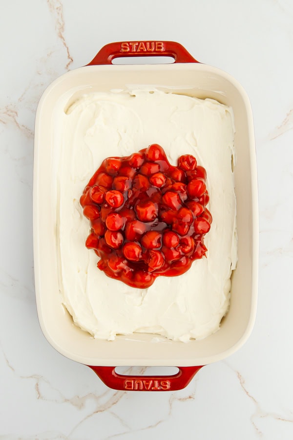 Cherry pie filling being spread over the cheesecake dip.