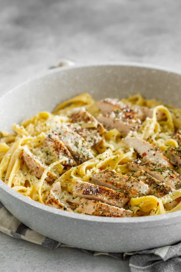Chicken Fettuccine Alfredo in a pan with sliced chicken breast on top of the pasta.