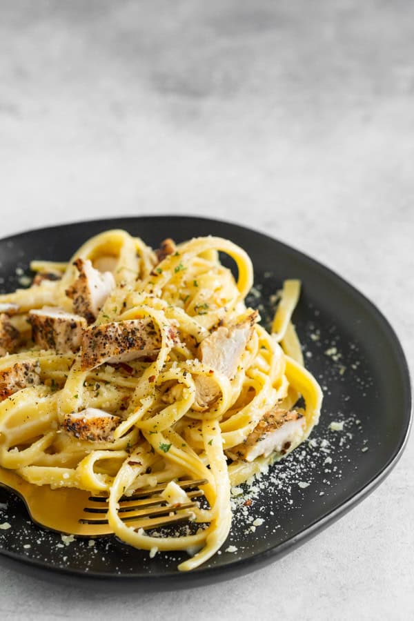 Chicken Fettuccine Alfredo on a black plate with a fork.