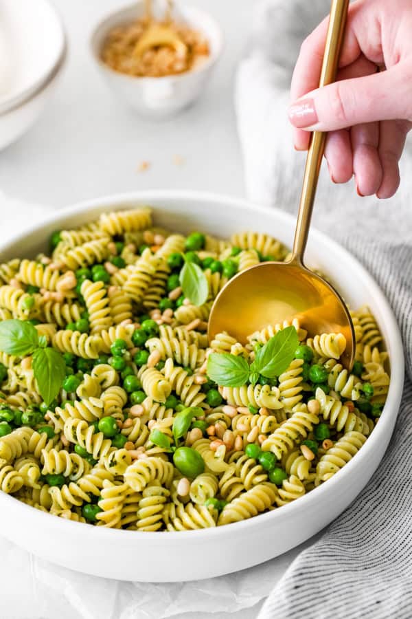 Pesto Pasta Salad getting scooped out of a serving bowl. 