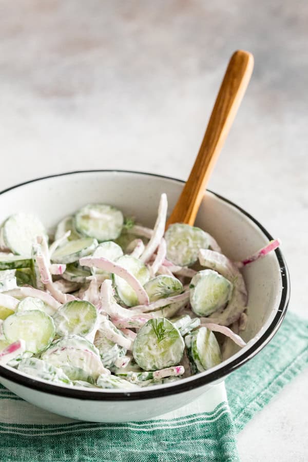 Creamy Cucumber Salad in a bowl with a wooden spoon.