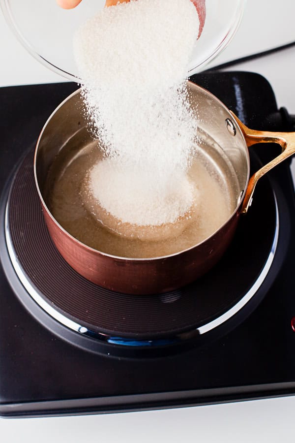 Pouring sugar into water to make mint simple syrup.