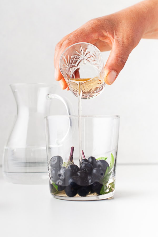 Pouring mint simple syrup into a cocktail.