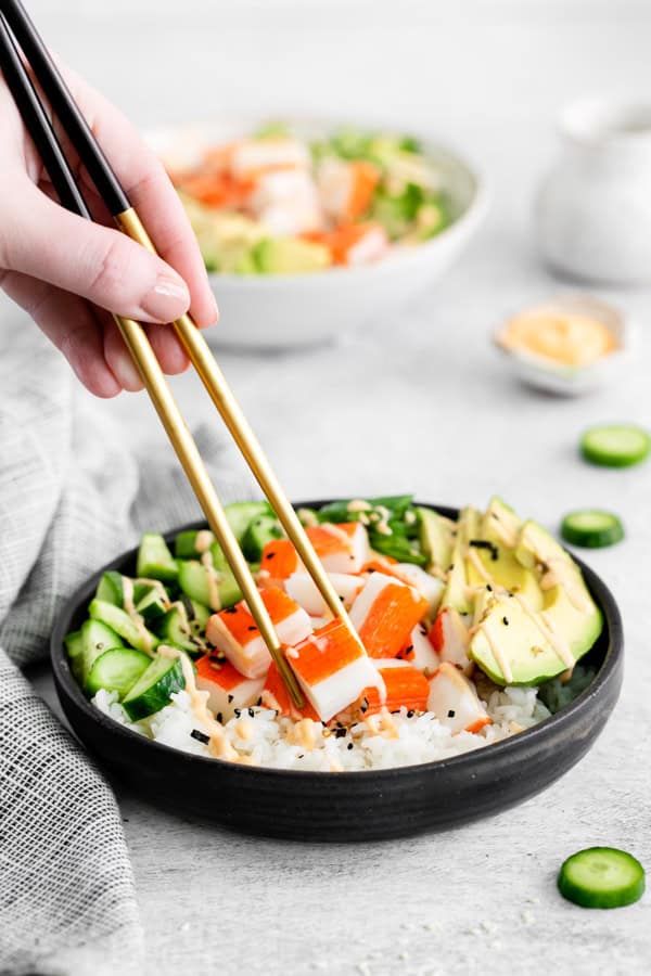 Chop sticks picking up a piece of crab from a sushi rice bowl.
