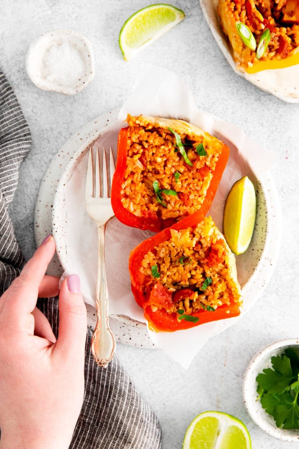 A hand holding the side of a plate with a cut in half stuffed bell pepper. 