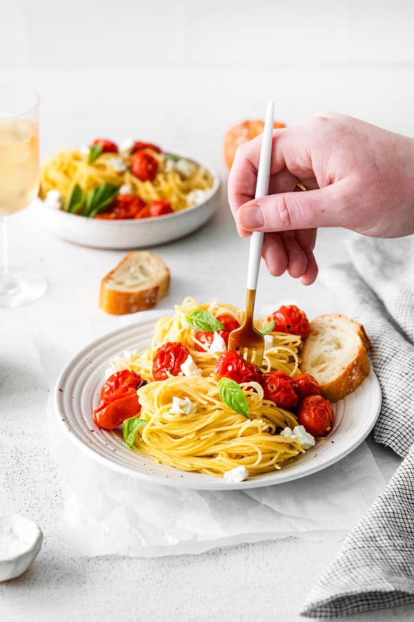 Roasted Tomato Goat Cheese Pasta on a plate with a hand twirling up the pasta. 