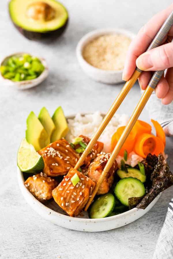 Chopsticks picking up a piece of salmon from a Teriyaki Salmon Bowl.