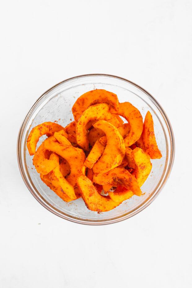 Pumpkin slices in a bowl tossed in seasoning. 