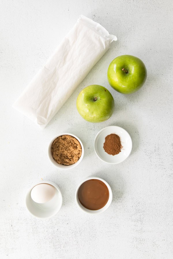 puff pastry, apples, cinnamon and sugar on a table.