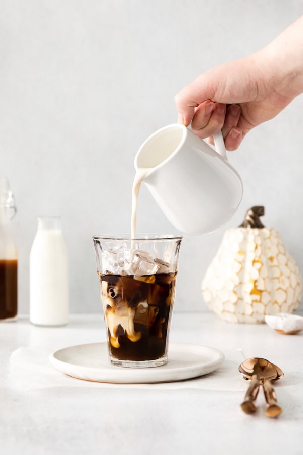 Pouring milk into a glass of Iced Pumpkin Chai Latte.