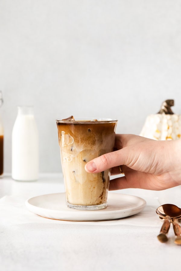 Iced Pumpkin Chai Latte in a glass with a hand holding the glass.