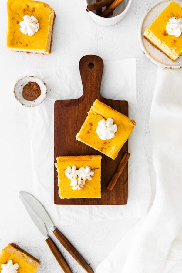 Pumpkin Cheesecake Bars on a wooden cutting board. 