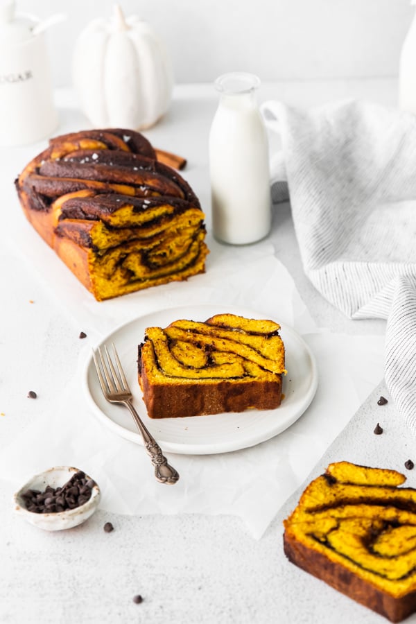 Pumpkin Chocolate Babka sliced on a white plate with the full loaf in the background. 