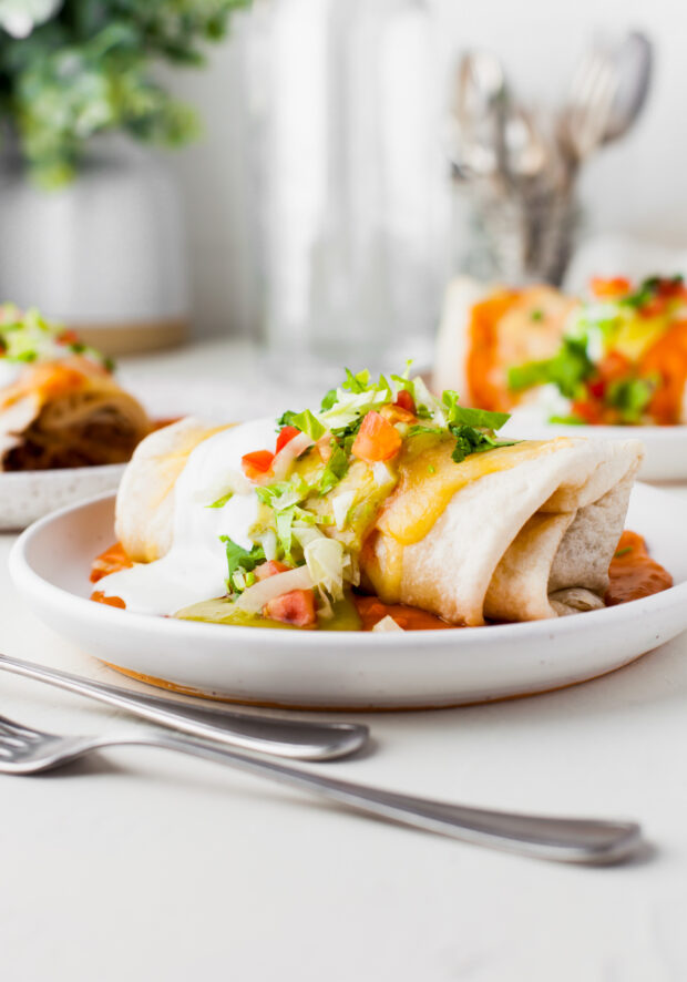 Smothered Burritos on a plate topped with cheese and lettuce. 