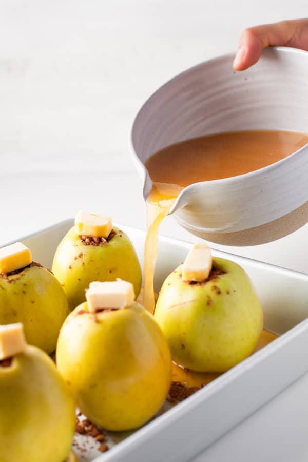 Cinnamon Baked Apples in a dish getting liquid poured into the dish. 