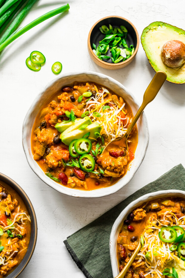 Turkey Pumpkin Chili in a bowl topped with avocado, cheese, and sliced jalapeno. 