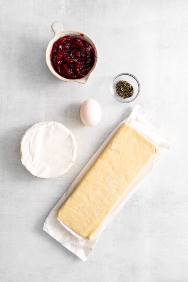 Puff pastry, Brie cheese, egg, herbs, and cranberry sauce on a table. 