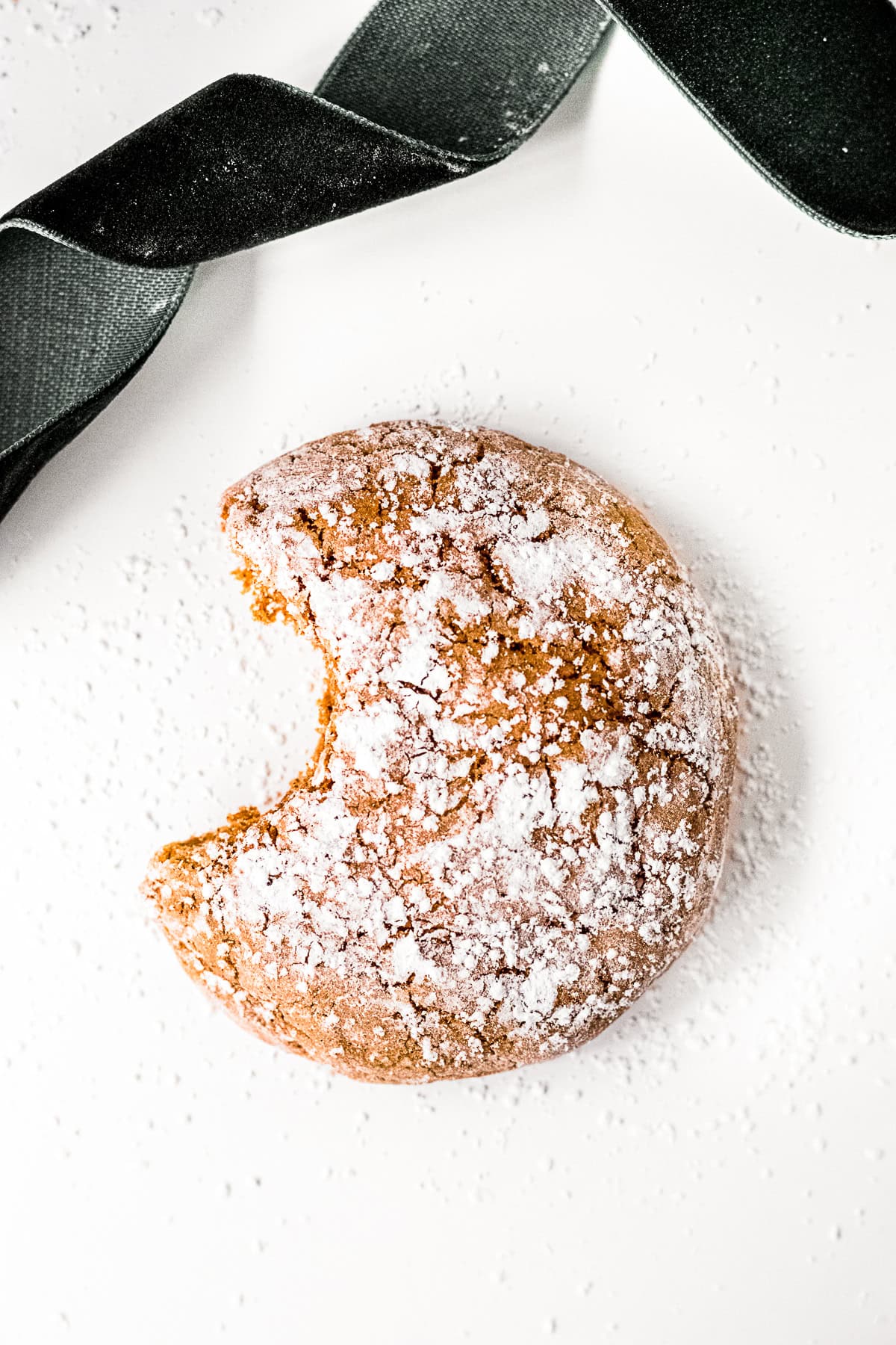Molasses Crinkle Cookies with a bite take out of it sitting on a table.