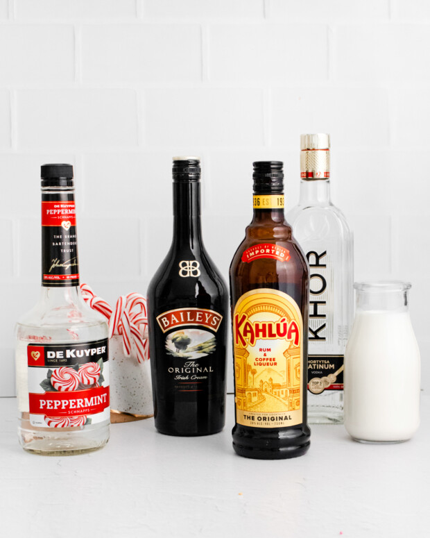 Peppermint schnapps, Baileys, Kahlua, vodka, and half and half sitting on a table. 