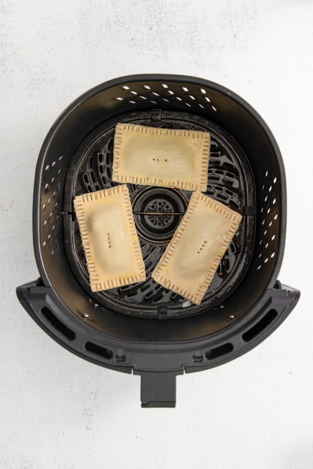 Uncooked air fryer pop tarts in a air fryer basket. 