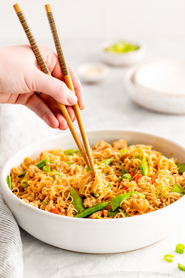 A hand using chop sticks picking up ramen noodle stir fry. 