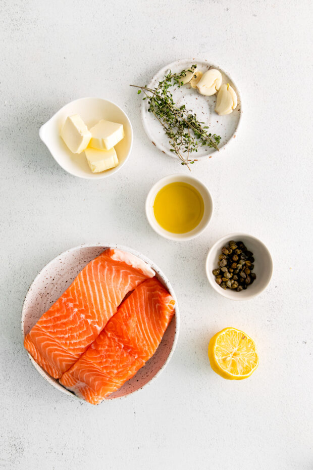 Salmon filets, lemon, butter, and thyme on a table.
