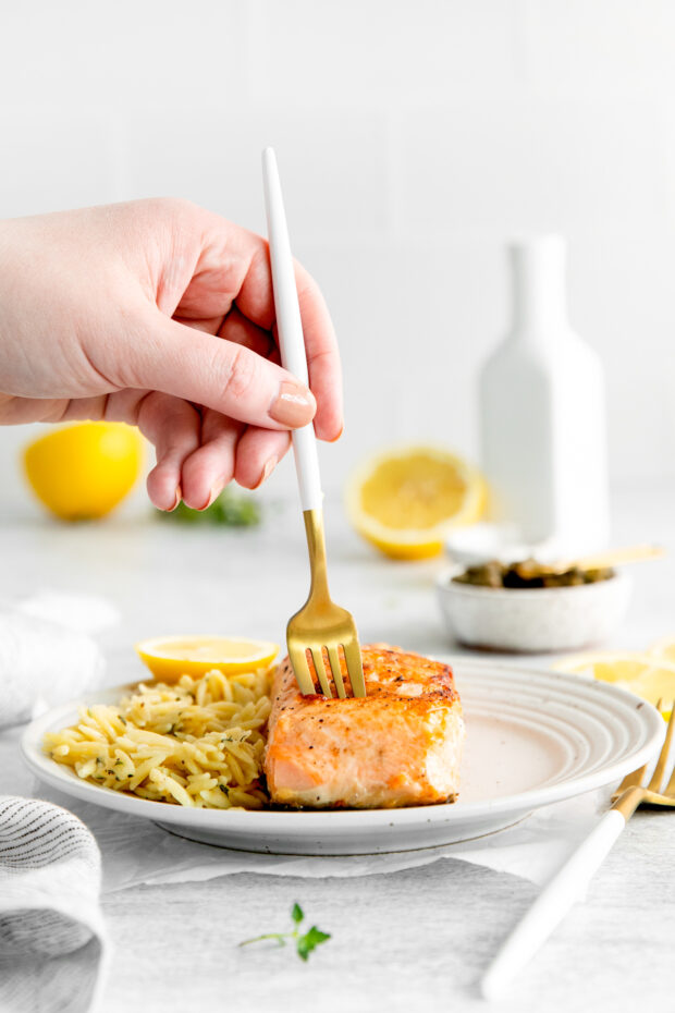 A hand holding a fork going into a piece of pan seared salmon.