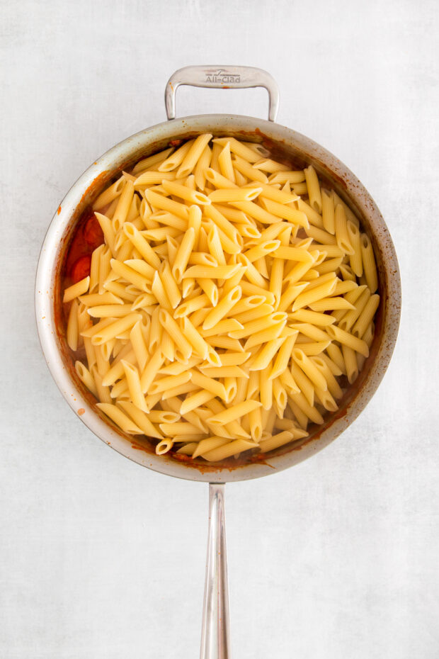 Penne pasta in a skillet over tomato sauce. 