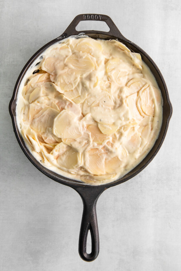 Uncooked scalloped potatoes in a skillet.