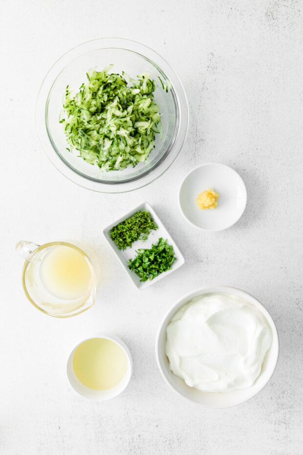Shredded cucumber, greek yogurt, and herbs on a table.