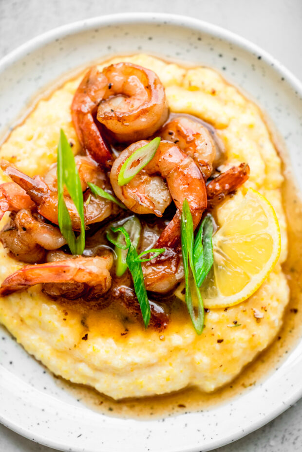 Cajun Honey Butter Shrimp and Grits served with lemon and green onions.