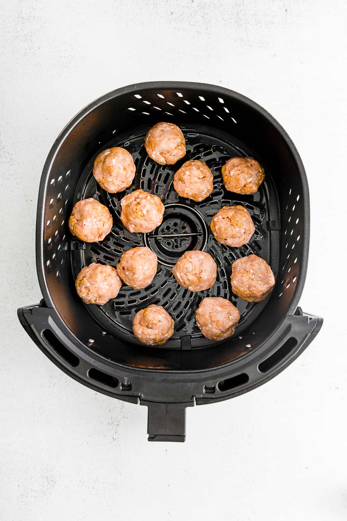 Uncooked air fryer chicken meatballs in a air fryer basket. 