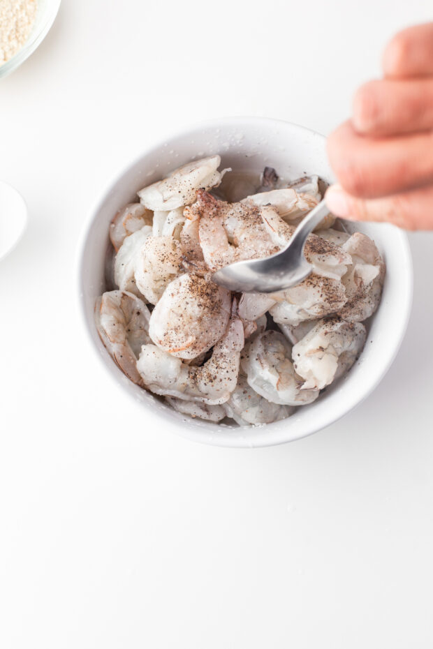 shrimp getting tossed in spices and lime juice in a bowl.