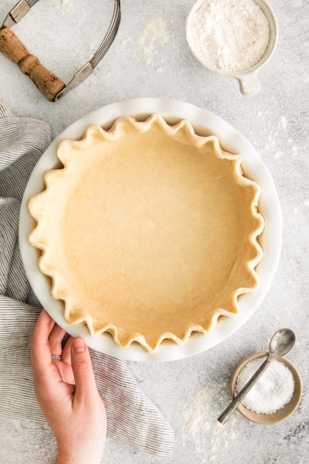 A hand holding a pie dish with an uncooked pie crust.