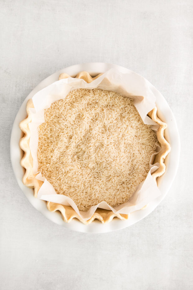 An uncooked pie crust with parchment paper in it with rice to help weight it down.