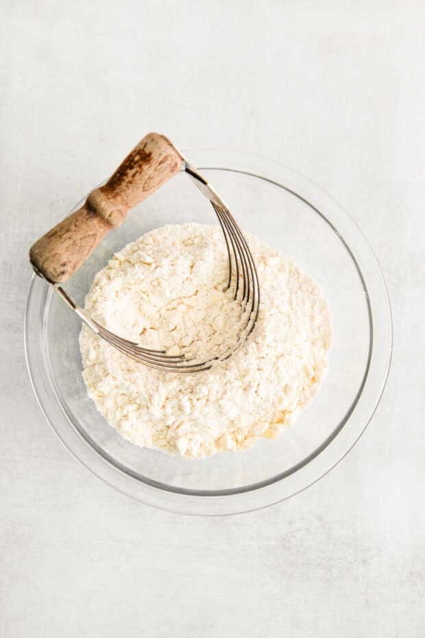 A bowl with flour and butter and a pastry cutter in it.